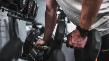 person in gray shirt holding black dumbbell