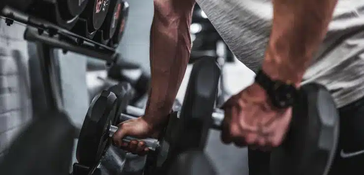 person in gray shirt holding black dumbbell