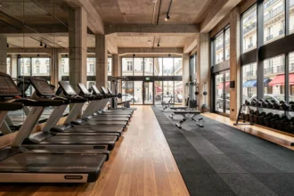 Vue panoramique d'une salle de fitness moderne à Paris avec équipements professionnels et grandes fenêtres donnant sur un boulevard haussmannien