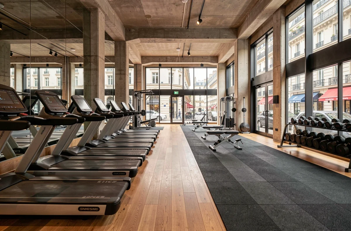 Vue panoramique d'une salle de fitness moderne à Paris avec équipements professionnels et grandes fenêtres donnant sur un boulevard haussmannien